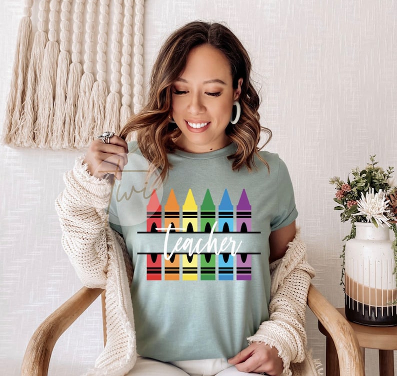 May include: A teal blue t-shirt with a rainbow of crayons and the word "Teacher" in a split monogram style.