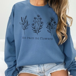 May include: A blue sweatshirt with a graphic of three different flowers and the text "no rain no flowers".