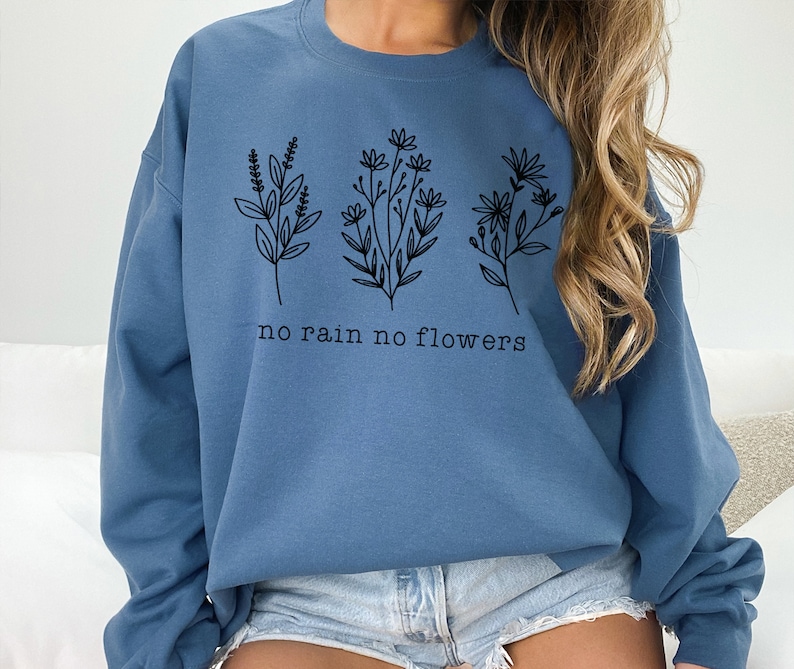 May include: A blue sweatshirt with a graphic of three different flowers and the text "no rain no flowers".