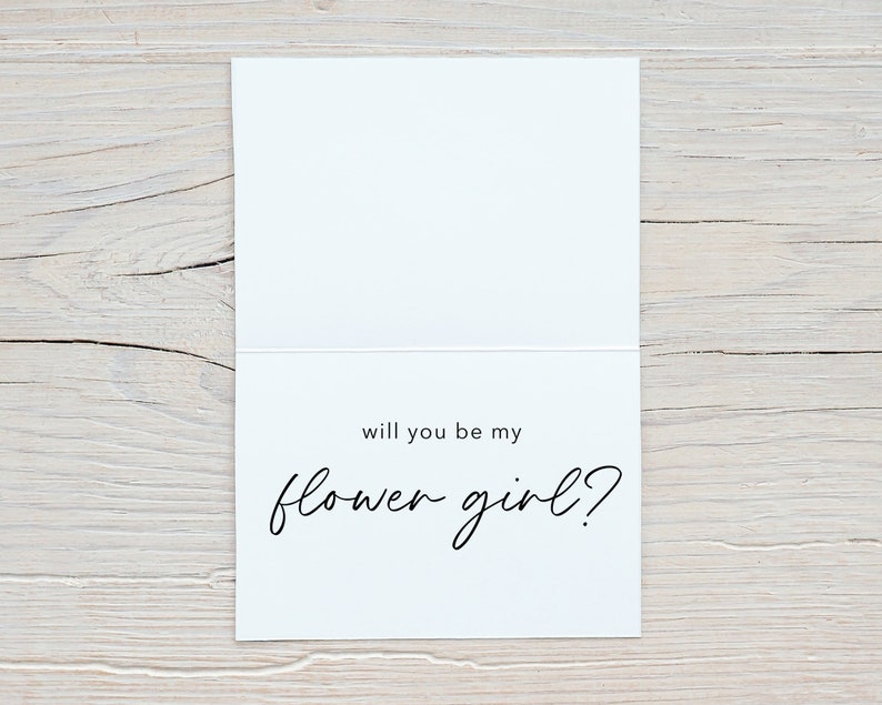 May include: A white card with black text that reads "Will you be my flower girl?"