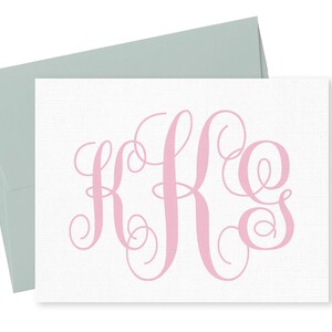 以下が含まれることがあります： 白いカードに、ピンク色の「KFS」のモノグラムが、筆記体で書かれています。