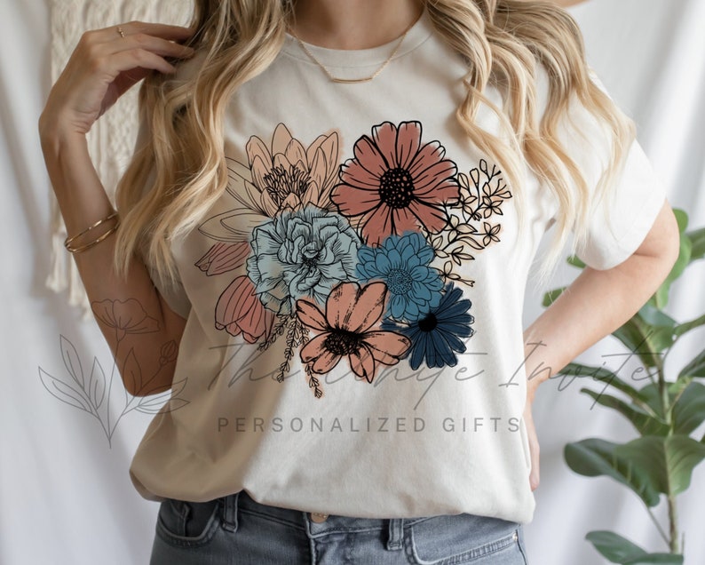 May include: A white t-shirt featuring a floral design with pink, peach, blue, and green flowers. The text "Personalized Gifts" is printed on the bottom of the shirt.