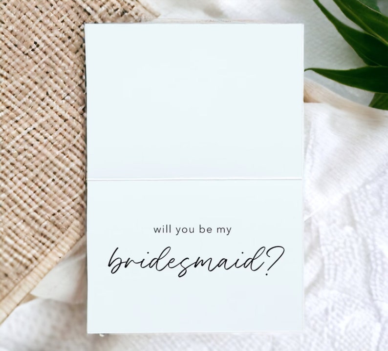 May include: A white card with black text that reads "Will you be my bridesmaid?"