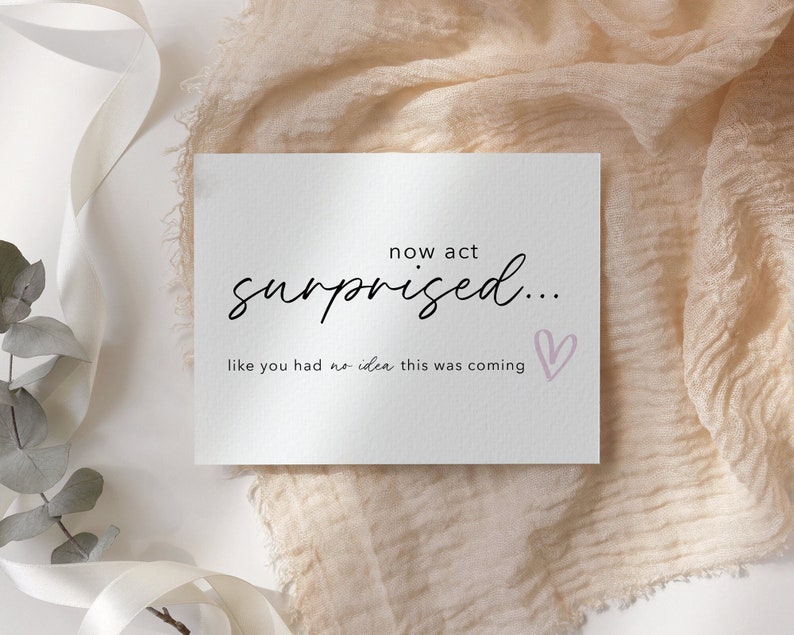 May include: A white card with black text that reads "now act surprised... like you had no idea this was coming" with a pink heart drawn on the right side.