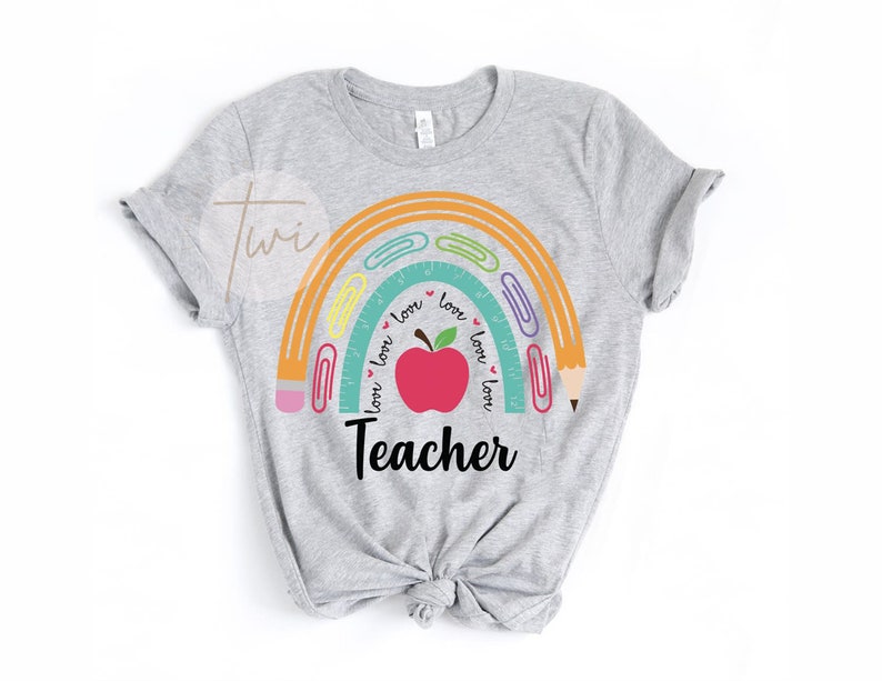 May include: Gray t-shirt with a rainbow design featuring a red apple, pencils, and paper clips. The rainbow has the words "love" written around it. The text "Teacher" is below the rainbow.