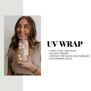 May include: A clear glass can tumbler with a bamboo lid and straw, decorated with a UV wrap featuring a pattern of pink bows and cream-colored flowers. The text "UV WRAP" is displayed.