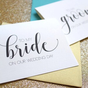 May include: Two white cards with black calligraphy. The card on the left says "To my bride on our wedding day". The card on the right says "To my groom on our wedding day".