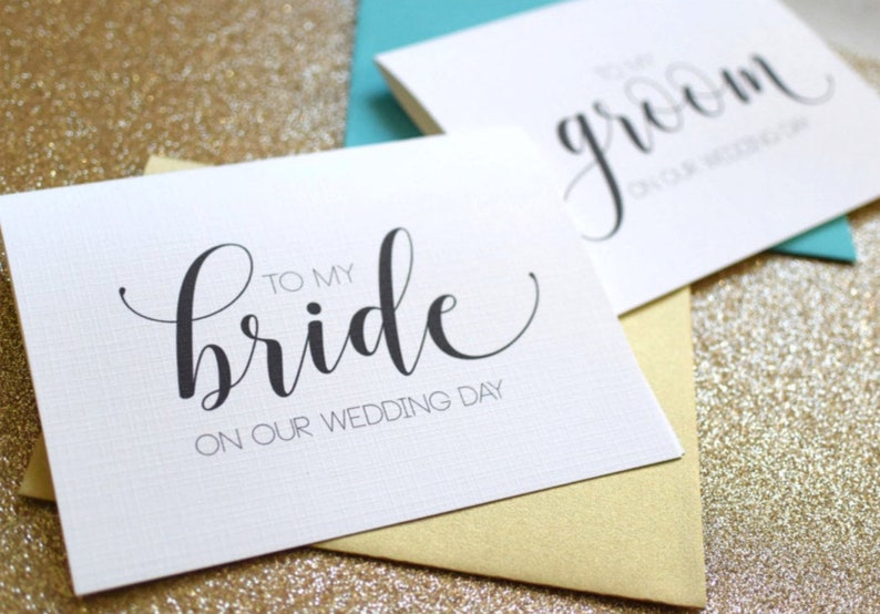 May include: Two white cards with black calligraphy. The card on the left says "To my bride on our wedding day". The card on the right says "To my groom on our wedding day".