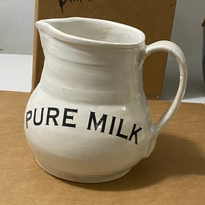 Puede incluir: Jarro de cerámica blanco con una inscripción negra que dice "PURE MILK".