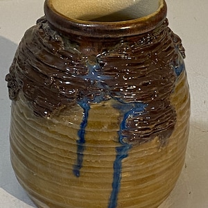 Puede incluir: Un jarrón de cerámica marrón con esmalte azul que gotea por los lados. El jarrón tiene una superficie texturizada y una abertura ancha.