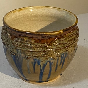 Puede incluir: Un cuenco de cerámica marrón con un esmalte blanco en el interior y un esmalte azul y marrón en el exterior. El cuenco tiene un diseño texturizado alrededor del borde.