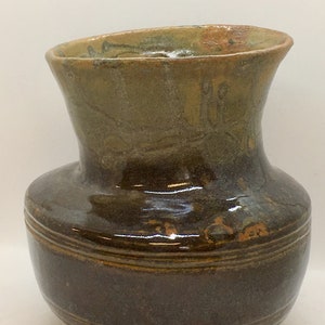 May include: A brown ceramic vase with a flared opening and a glossy finish. The vase has a light brown rim and a band of light brown around the bottom.