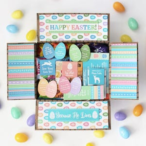 May include: An open cardboard box decorated with pastel Easter-themed patterns and text. The box contains various Easter-related items, including colorful egg-shaped cards, a small bunny illustration, and chocolate eggs. The box is surrounded by scattered plastic Easter eggs.