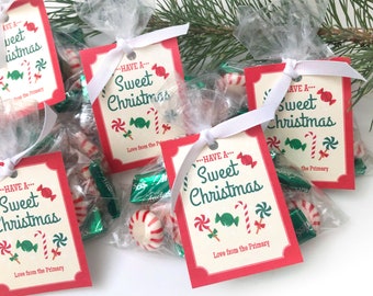 Könnte beinhalten: Rote und weiße Geschenktüten mit durchsichtigen Cellophanfenstern, gefüllt mit Süßigkeiten. Jede Tüte hat ein weißes Band und ein rotes und weißes Etikett mit der Aufschrift "Have a Sweet Christmas" mit einem Zuckerstangen- und Lutscherdesign. Das Etikett trägt außerdem die Aufschrift "Love from the Primary".