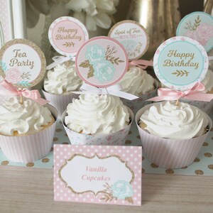 May include: Vanilla cupcakes decorated with pink and blue frosting and topped with gold glitter cupcake toppers that say "Tea Party", "Happy Birthday", and "Spot of Tea with the Tea Girl".