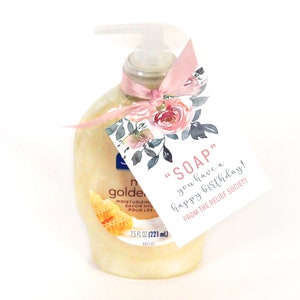 May include: A clear bottle of liquid hand soap with a pink ribbon and a floral tag that reads "SOAP you have a happy birthday! FROM THE RELIEF SOCIETY".