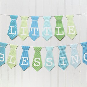 Può includere: Uno striscione di carta blu e verde con le parole "Little Blessing" scritte in lettere bianche su una corda di ritagli di carta a forma di cravatta.