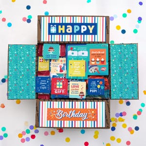 以下が含まれることがあります： 誕生日をテーマにした様々なカードやギフトが入った、開いた段ボールのギフトボックス。ボックスはカラフルなストライプで装飾され、「Happy」と「Birthday」の文字が書かれています。ボックスの周りには紙吹雪があります。