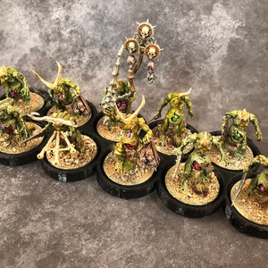 Peut inclure: Un groupe de 12 figurines miniatures peintes en vert et brun avec des cornes et des armes, debout sur des socles noirs. Les figurines sont dispos&eacute;es en cercle autour d'une figurine centrale tenant un b&acirc;ton surmont&eacute; d'un cr&acirc;ne.