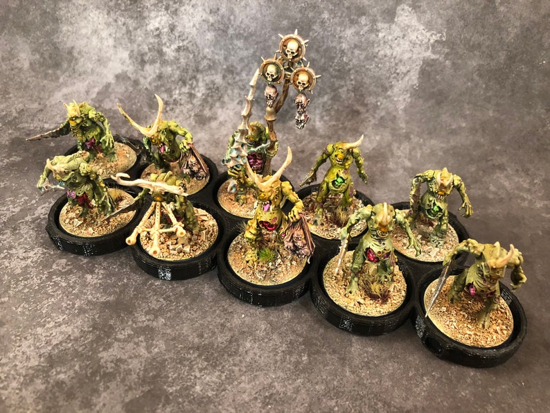 Peut inclure: Un groupe de 12 figurines miniatures peintes en vert et brun avec des cornes et des armes, debout sur des socles noirs. Les figurines sont dispos&eacute;es en cercle autour d'une figurine centrale tenant un b&acirc;ton surmont&eacute; d'un cr&acirc;ne.