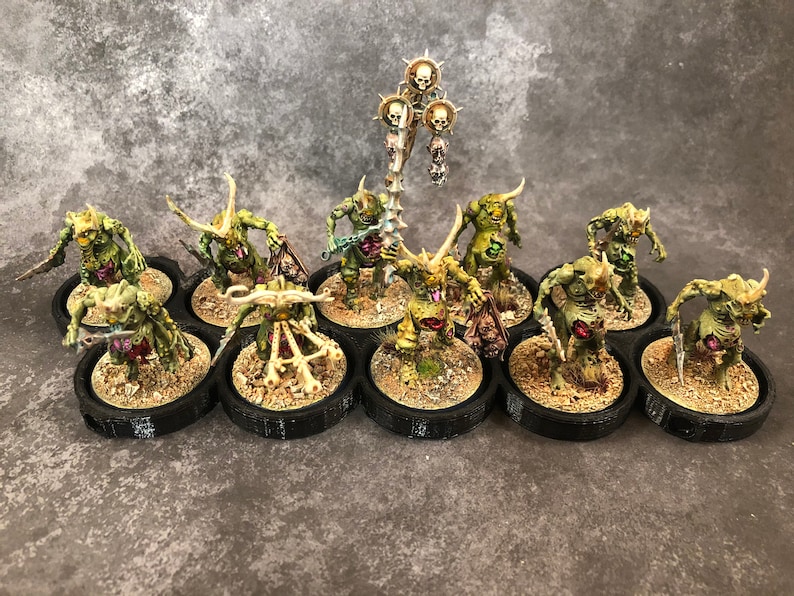Peut inclure: Un ensemble de 10 figurines miniatures peintes en vert et blanc avec des cornes et des armes, pos&eacute;es sur des socles noirs. Les figurines sont dispos&eacute;es en cercle autour d'une figurine centrale avec un b&acirc;ton surmont&eacute; d'un cr&acirc;ne.