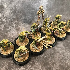 Peut inclure: Un groupe de dix figurines miniatures peintes en vert et brun avec des &eacute;p&eacute;es et des armes en os sur des socles noirs. Les figurines sont dispos&eacute;es en ligne et sont pr&ecirc;tes pour le combat.