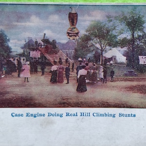 May include: Vintage postcard depicting a Case engine performing hill climbing stunts. The image shows a crowd of people watching the demonstration. Text on the postcard reads "Case Engine Doing Real Hill Climbing Stunts" and "Case Engines are the only real Hill Climber."