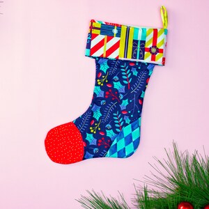 May include: A blue and red Christmas stocking with a holly and leaf pattern. The stocking has a red cuff with a colourful pattern of presents and stripes.