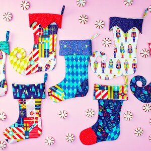 May include: A collection of six colourful Christmas stockings with various patterns, including a nutcracker design, a geometric pattern, and a Christmas tree design. The stockings are arranged on a pink background with candy canes scattered around them.