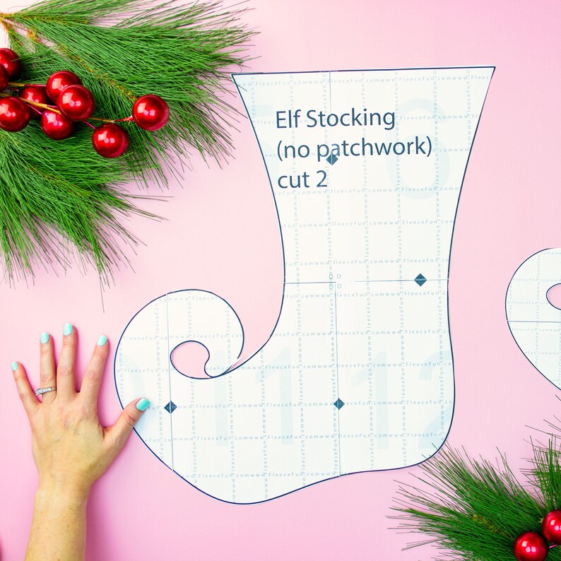 May include: A white elf stocking pattern on a pink background. The pattern is on a grid and includes the text "Elf Stocking (no patchwork) cut 2".