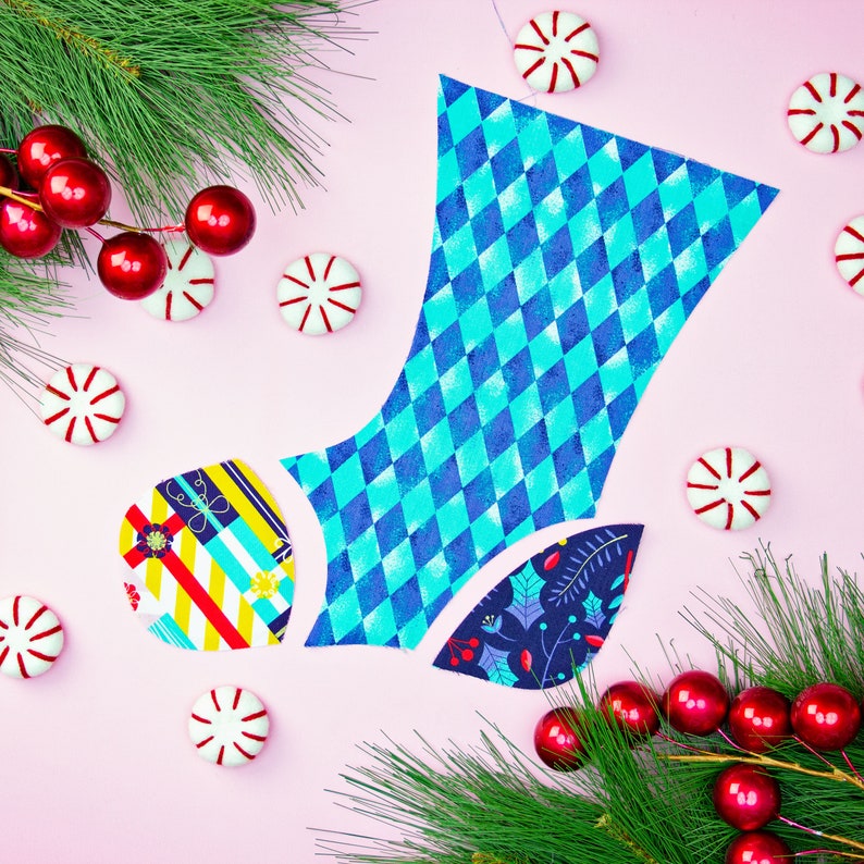 May include: A blue and white diamond patterned fabric boot with a red and yellow striped fabric boot and a blue and green floral fabric boot. The boots are surrounded by red and white candy canes and a green pine branch.