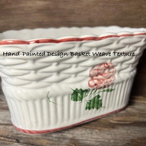 May include: White ceramic planter with a basket weave texture and hand-painted floral design. The rim is trimmed with red paint. The text "Hand-Painted Design Basket Weave Texture" is printed on the front.