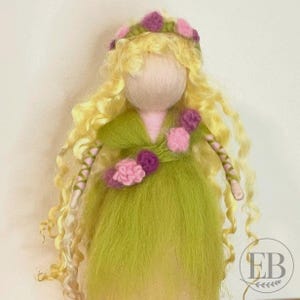 May include: A handmade doll with a light green dress and long, curly blonde hair. The doll has a flower crown and pink and purple floral accents. The doll's arms are wrapped with pink and green yarn. The doll has a blank face.