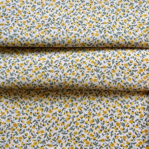 Könnte beinhalten: Ein weißer Stoff mit einem dichten, sich wiederholenden Muster aus kleinen gelben Blüten mit grünen Stielen und Blättern. Das Design ist gleichmäßig über die gesamte Oberfläche verteilt und erzeugt ein durchgehendes florales Motiv.