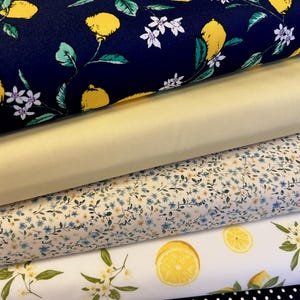 May include: A selection of patterned fabrics. The top fabric is navy blue with yellow lemons, white flowers, and green leaves. Beneath is a plain light yellow fabric, followed by a floral pattern, a lemon print, and a black and white polka dot fabric.