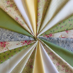 May include: A collection of fabric swatches arranged in a circular fan pattern, featuring various patterns including pink roses on cream, white polka dots on light green, solid yellow, blue floral prints, and solid olive green cotton textiles.