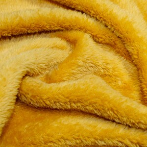 K&ouml;nnte beinhalten: Nahaufnahme eines weichen, gelben Kunstpelzes. Der Stoff hat eine flauschige Textur und eine warme, einladende Farbe.