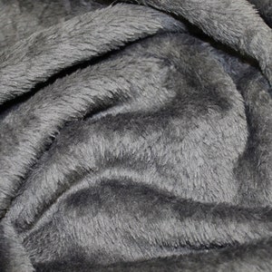 K&ouml;nnte beinhalten: Nahaufnahme eines weichen, grauen, pl&uuml;schigen Stoffes mit einer flauschigen Textur. Der Stoff ist gefaltet und drapiert, wodurch die Textur und Weichheit sichtbar werden.