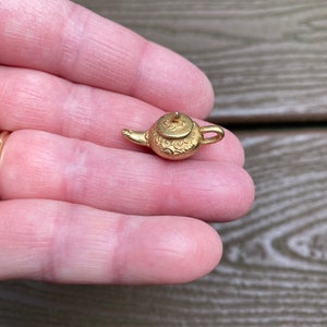 Könnte beinhalten: Ein kleiner goldener Teekannen-Anhänger mit einem detaillierten Design. Der Anhänger ist etwa so groß wie eine 10-Cent-Münze.