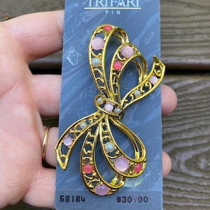 Joyería vintage firmada por Trifari. Hermoso lazo dorado con cabujones rosas y broche de perlas. Nuevo en caja.