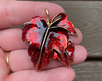 Peut inclure: Broche en forme de feuille rouge et dorée. La broche a une finition brillante et pailletée avec une tige et des bords dorés. La feuille est de couleur rouge foncé avec des accents rouges plus foncés.
