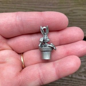 May include: A silver charm featuring Bugs Bunny peeking out of a flower pot. The charm has a loop at the top for attaching to a necklace or bracelet.