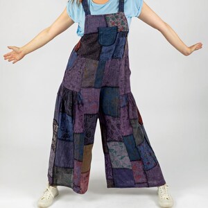 Könnte beinhalten: Lila Patchwork-Jumpsuit mit weiten Beinen. Der Jumpsuit besteht aus verschiedenen gemusterten Stoffquadraten in Lila-, Blau- und Brauntönen. Das Model trägt ein hellblaues T-Shirt und weiße Turnschuhe.