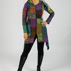 May include: A long, patchwork hooded jacket in various colours, including purple, green, and brown. The jacket features a zip closure and is worn with black leggings and knee-high black boots. The overall style is bohemian.