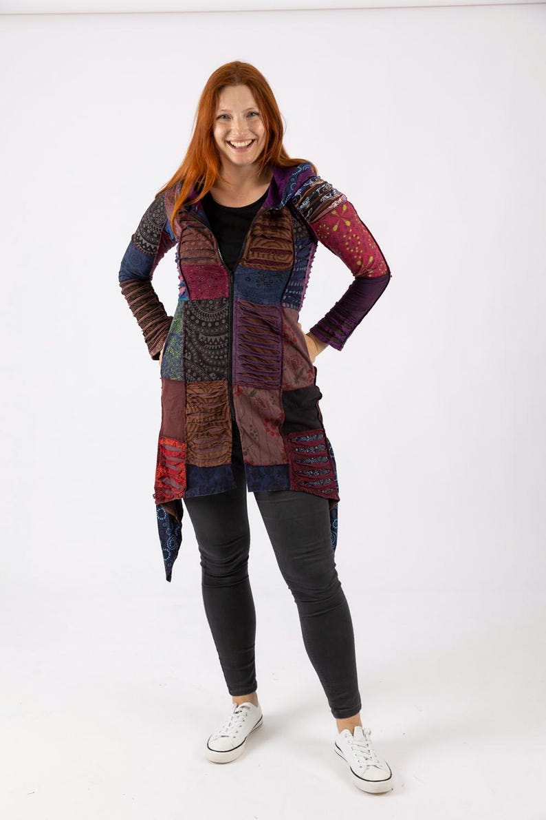 May include: A long patchwork jacket with a zip fastening. The jacket displays a variety of colours and patterns, including blue, red, purple, and brown. The sleeves are long and the jacket is worn with black trousers and white trainers.