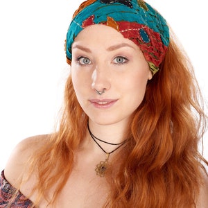 Puede incluir: Una mujer con el pelo largo y ondulado de color rojo que lleva una diadema con estampado colorido. Lleva un collar negro de gargantilla con un colgante dorado y un top de hombros descubiertos con estampado negro y rojo.