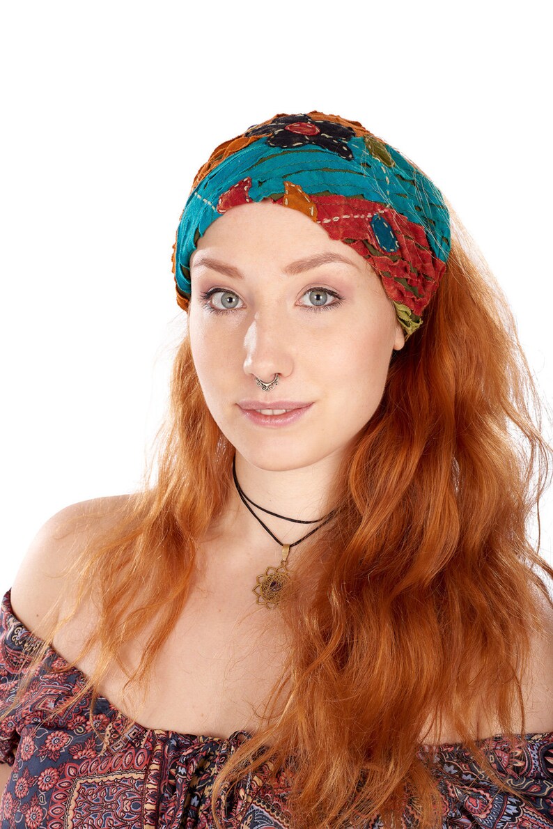 Puede incluir: Una mujer con el pelo largo y ondulado de color rojo que lleva una diadema con estampado colorido. Lleva un collar negro de gargantilla con un colgante dorado y un top de hombros descubiertos con estampado negro y rojo.