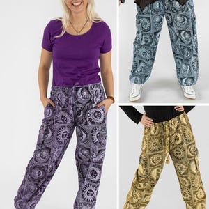 Könnte beinhalten: Drei gemusterte Cargohosen sind abgebildet. Eine Hose ist lila, eine andere blau und die dritte goldfarben. Jede Hose hat ein sich wiederholendes Sonnen- und Monddesign. Die Hosen haben Taschen und einen Kordelzug in der Taille. Die Models tragen weiße Turnschuhe.