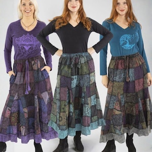 Può includere: Tre donne indossano top a maniche lunghe e gonne patchwork. I top sono viola, neri e verde acqua, ognuno con una grafica diversa. Le gonne sono realizzate con quadrati fantasia in tonalità viola, verdi e blu. Le donne indossano stivali neri.