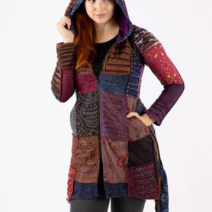 May include: A patchwork hooded jacket in shades of brown, purple, and blue. The jacket features a zip closure, pockets, and a hood with a contrasting lining. The sleeves and body are made of various patterned fabrics.